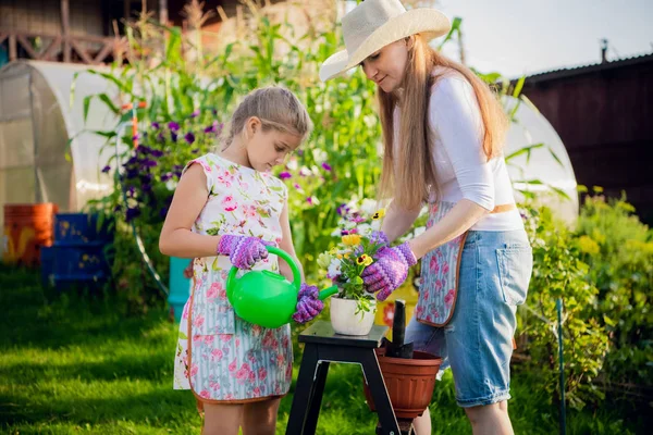 Femme jardinier aider sa fille à verser pot de fleurs de jardin . — Photo