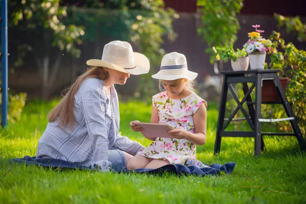 Ευτυχισμένη μητέρα και η μικρή της κόρη απολαμβάνουν δωρεάν χρόνο χρησιμοποιώντας tablet υπολογιστή ενώ χαλαρώνετε στον κήπο σπιτιού διακοπών κατά τη διάρκεια της ηλιόλουστη μέρα. — Φωτογραφία Αρχείου