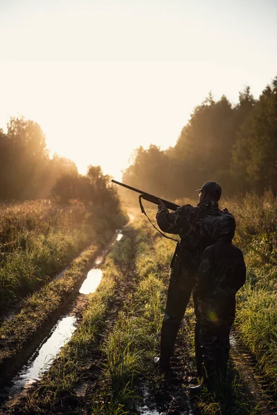 Vadászfelszereléssel rendelkező vadászok, akik a vadászidény alatt vidéken, napnyugtakor a mezőn keresztül az erdő felé tartanak.. — Stock Fotó