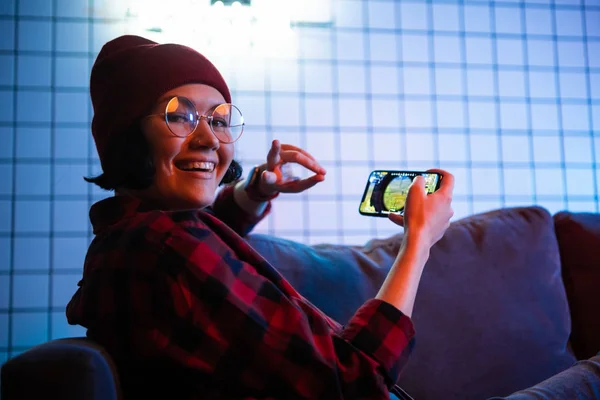 Adolescente chica emocionante jugando teléfono inteligente en una habitación iluminada con color neón en casa . — Foto de Stock