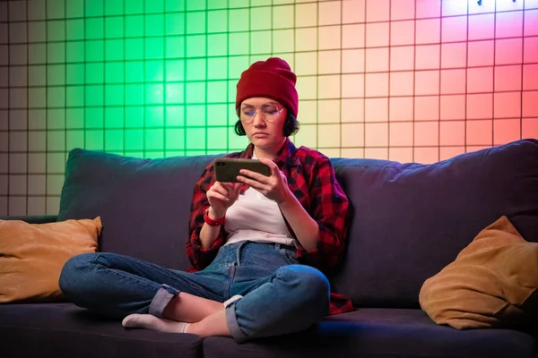 Портрет молодой девушки хипстера подростка с помощью смартфона на диване с подушками в интерьере гостиной — стоковое фото