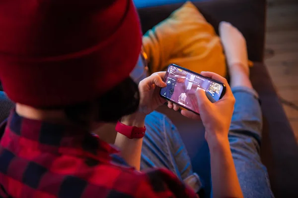 MOSCÚ, RUSIA - Diciembre 2019: vista trasera de un primer plano de una mujer jugando juego en línea en un teléfono inteligente tumbado en un sofá en casa — Foto de Stock