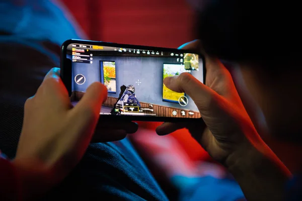 MOSCÚ, RUSIA - Diciembre 2019: vista trasera de un primer plano de una mujer jugando juego en línea en un teléfono inteligente tumbado en un sofá en casa —  Fotos de Stock