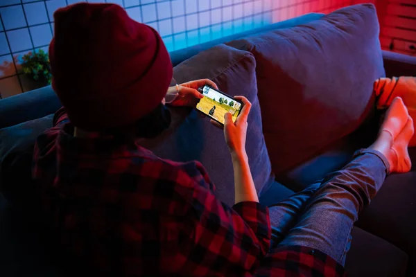 Moskau, russland - dezember 2019: rückseite einer nahaufnahme einer hände einer frau, die online-spiel auf einem smartphone spielt, liegend auf einer couch zu hause — Stockfoto