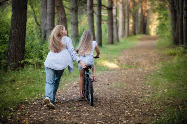 Anne çocuğunu bisiklete binmeye götürüyor. Bisiklete ilk biniş için yardım.