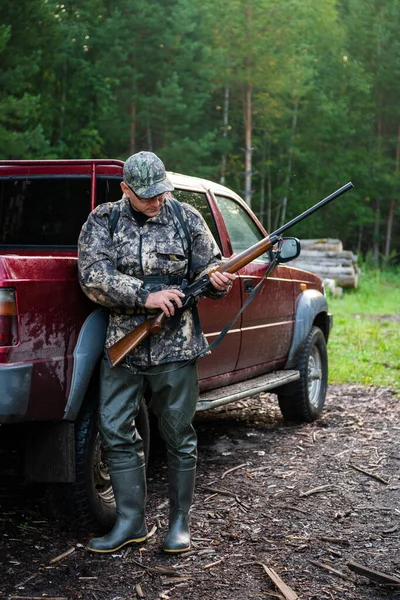 Hunter samec nabíjecí pistole, na sobě příležitostné lovecké oblečení, pažba a nůž na dolní části zad. Pozadí lesa. — Stock fotografie