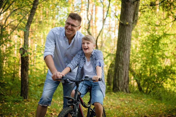 Jeune père enseignant à son fils souriant comment faire du vélo — Photo