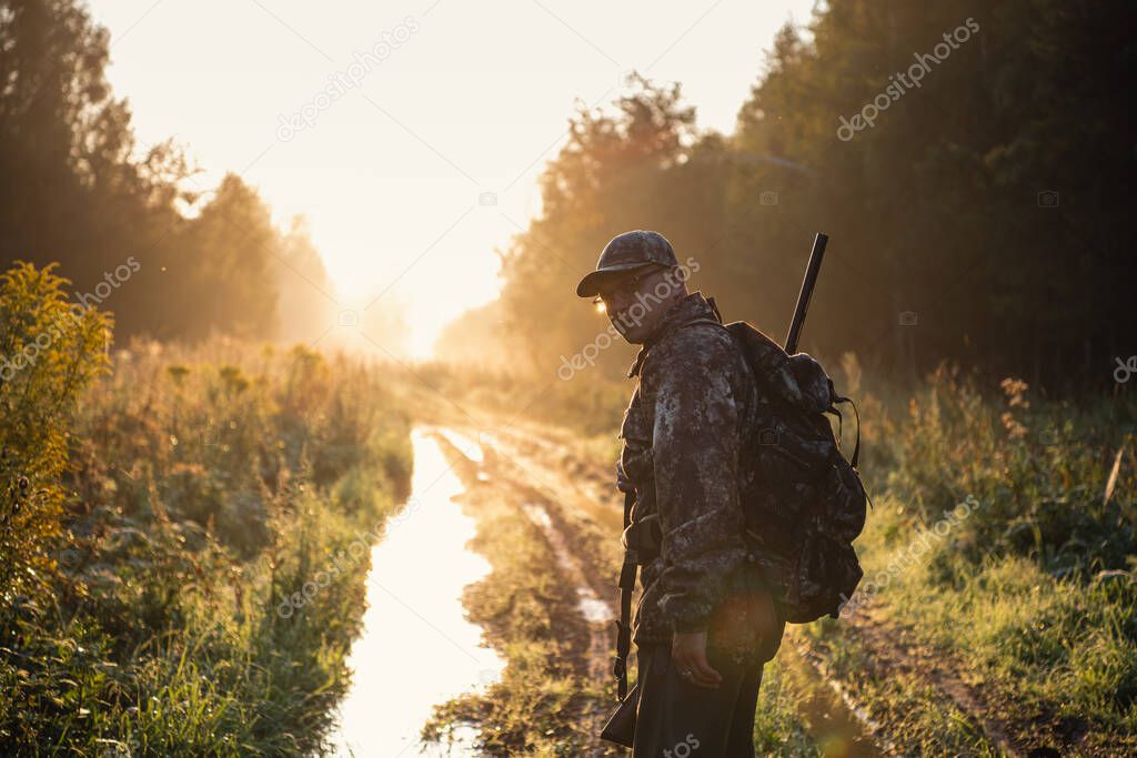 Silhouette of a hunter on the background of the morning red dawn. Stands at the ready with a gun.