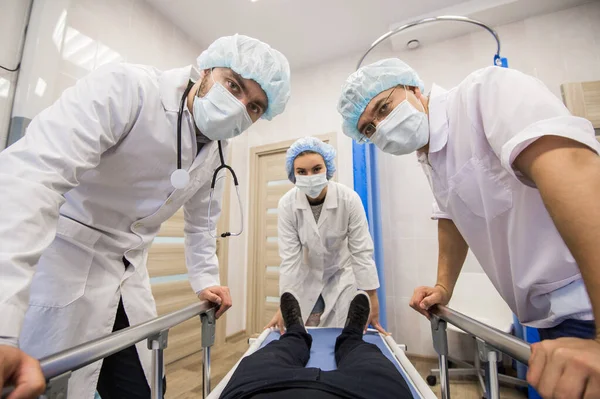 Lékaři v virových ochranných bílých maskách se dívají do kamery shora jako vy jako pacient. Pracují na tom, jak zastavit epidemii korony viru.. — Stock fotografie