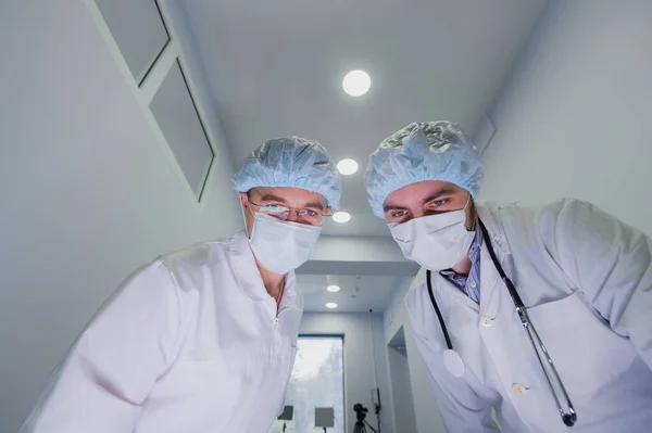 Los médicos con un traje de protección viral, con máscaras blancas, miran a la cámara desde arriba como si fueras un paciente. Están trabajando en cómo detener la epidemia de la corona del virus . — Foto de Stock