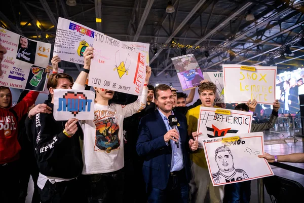 Μόσχα - 23 Δεκεμβρίου 2019: esports επαγγελματική εκδήλωση τυχερών παιχνιδιών. Newsman με μικρόφωνο συνέντευξη οπαδούς τυχερών παιχνιδιών που ζητωκραυγάζουν για τις αγαπημένες ομάδες που διαμένουν στη ζώνη ανεμιστήρα και κρατώντας μεγάλες αφίσες — Φωτογραφία Αρχείου
