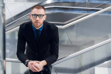 Elinde çantasıyla merdivenlerde duran zarif genç bir adam. Kameraya bakıyor.