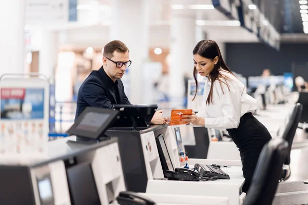 Zijaanzicht van een knappe man met een bril die een paspoort geeft aan het personeel bij het inchecken op de luchthaven — Stockfoto