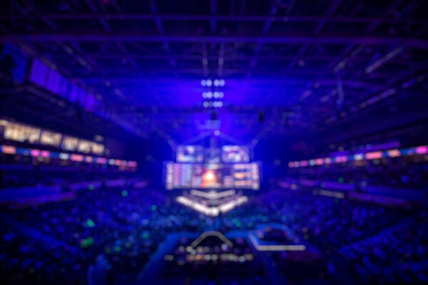 Blurred background of an esports event - Big illuminated main stage of a computer games tournament located on a big stadium. Tribunes are full of video games fans.