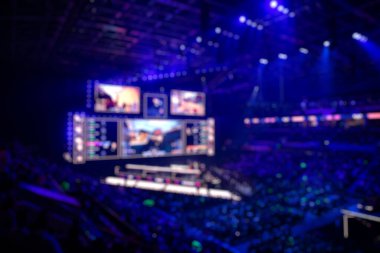 Esport etkinliğinin arka planında bulanıklık var. Büyük bir stadyumdaki bilgisayar oyunları turnuvasının büyük bir sahnesi aydınlandı. Tribünler video oyunu hayranlarıyla dolu..