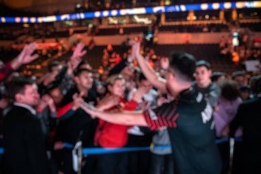 Esport etkinliğinin arka planı bulanık. Turnuva sahasında tribünde bir sürü hayranı olan kazanan oyuncu. Köklerine resim yapıp, imza dağıtıyor..