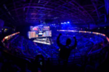 Esport etkinliğinin arka planında bulanıklık var. Büyük bir stadyumdaki bilgisayar oyunları turnuvasının büyük bir sahnesi aydınlandı. Tribünler video oyunu hayranlarıyla dolu..
