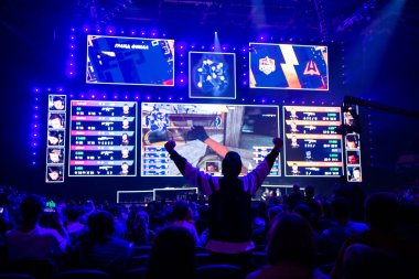 Büyük Esport etkinliği. Turnuva arenasında bir tribünde elleri havada bilgisayar oyunları hayranı. En sevdiği takım için tezahürat yapıyor..