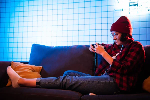 Retrato joven adolescente hipster chica usando el teléfono móvil inteligente en el sofá con almohadas en el interior de la sala de estar — Foto de Stock