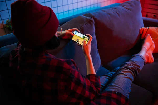 MOSKAU, RUSSLAND - 6. Dezember 2019: Seitenansicht eines Teenagers beim Online-Spiel PUBG auf einem Smartphone, das nachts zu Hause auf einem Sofa liegt. — Stockfoto