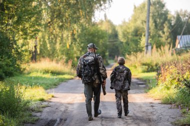 Avcı ekipmanlı avcılar kırsal alandan ormana doğru gidiyorlar. Gün batımında kırsal kesimde av mevsiminde..