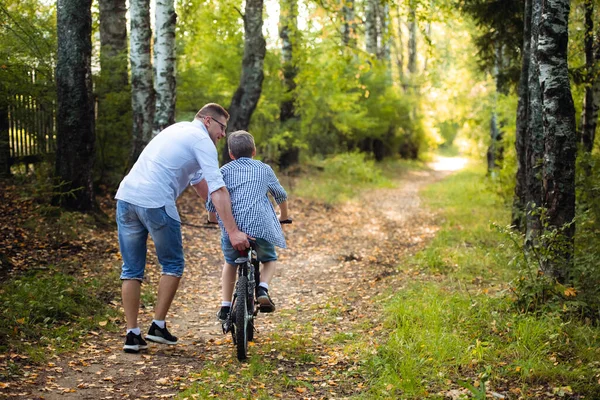 Jeune père enseignant à son fils souriant comment faire du vélo — Photo