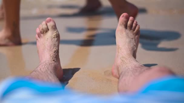 Ноги на песчаном пляже рядом с синей морской водой. 4K видеоклип — стоковое видео
