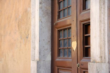 Roma 'nın eski evlerinden birinin eski kahverengi ahşap kapısı. Kapısında parmaklık olan bir pencere var. Kapıda kalp etiketi var.