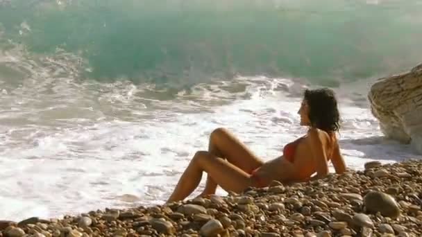 在沙滩上穿着泳装的年轻英俊的黑发女子放松了阳光 看着海浪在美丽的海面上湿润了她的身体 在阳光明媚的日子里 洛基海岸 — 图库视频影像