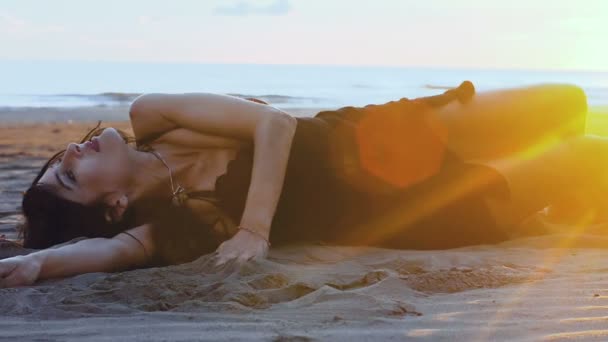 女人引诱和愉快地滚动沿着沙滩上的沙子 轻轻地笑 从附近和在背景 海洋和周围的日落可以看到一个镜头耀斑 — 图库视频影像