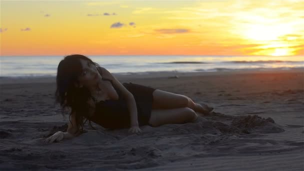 女人引诱和愉快地滚动沿沙滩上的沙子 从附近和背景 海洋和日落的环境可以看到 — 图库视频影像