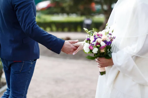 Detalhe de recém-casados, noiva e noivo, de mãos dadas e buquê de flores, vista lateral . — Fotografia de Stock