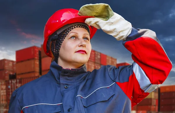 The woman in protective working clothes. labor protection .Under construction . Work safety .A helmet for protection of the head . A helmet for protection of the head .  Working gloves . Industrial protective wear . Stacked cargo containers in port
