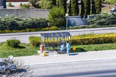 Koruyucu dezenfeksiyon kıyafeti giymiş bir kadın sterilizatör sıkar, insanların biriktiği yerlere. Profesyonel bir sanatoryum virüsün şehir sokaklarını temizliyor.