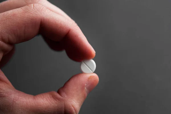 Beyaz bir hap koyu arka plan ilaç eczane sağlık üzerinde tutan el