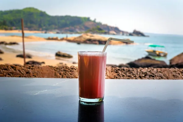 O coquetel de morango com uma palha em um copo está na mesa no fundo do mar . — Fotografia de Stock