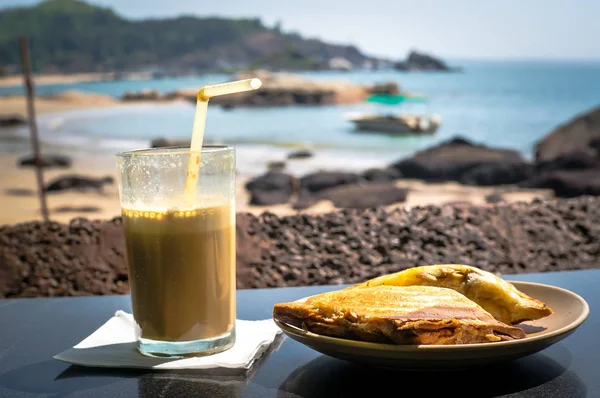 Ontbijt op het strand. Een broodje en een kop koffie cocktail op de tafel in het restaurant op de achtergrond van de zee — Stockfoto