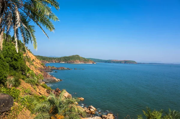 A táj is gyönyörű sziklás tengerpart, pálmafa, a kék tenger és a felhőtlen égen-Om beach, Karnataka, India — Stock Fotó