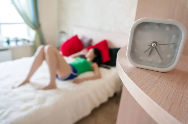 Relógio de alarme branco no fundo de dormir na cama menina no início da manhã . — Fotografia de Stock