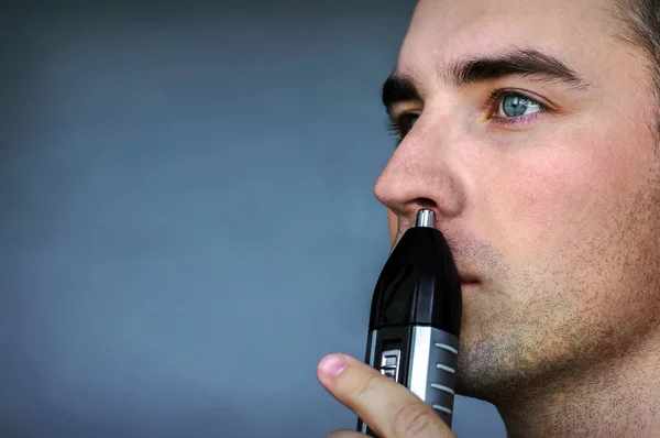 Handsome young man remove hair from his nose with trimmer — Stock Photo, Image