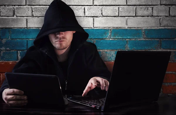 Un hacker seduto ad una scrivania con un computer e un tablet in mano — Foto Stock