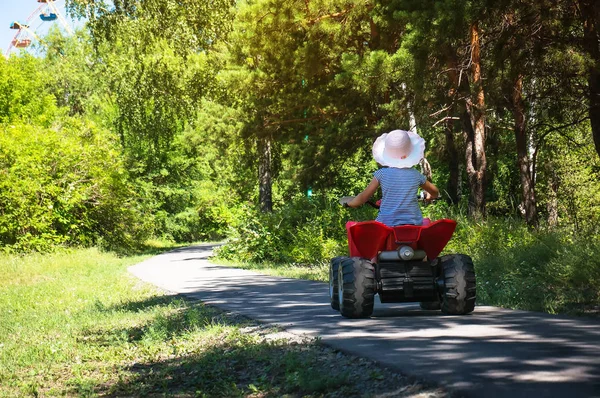 Baby flicka som rider på en röd Atv i en grönskande Park — Stockfoto