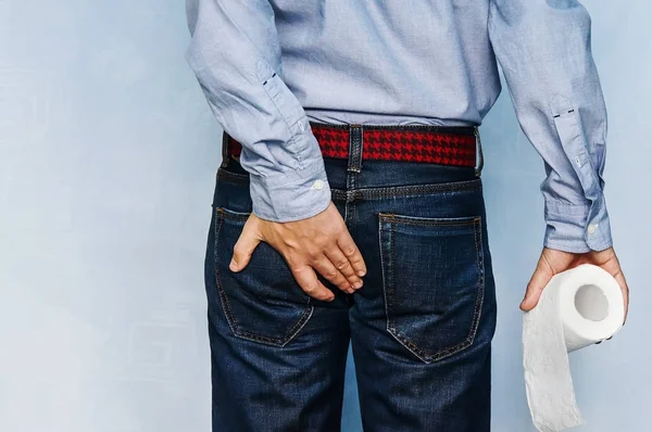 Homem segurando rolo de papel higiênico e segurando sua bunda no fundo azul . — Fotografia de Stock