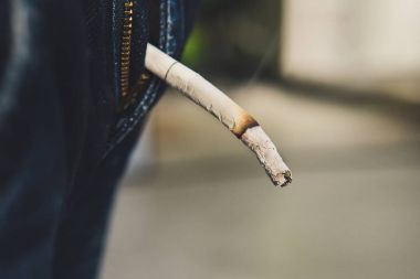 Adam üzerinden iki parmak ile Sigara İçilmeyen sigara izmariti tutar.