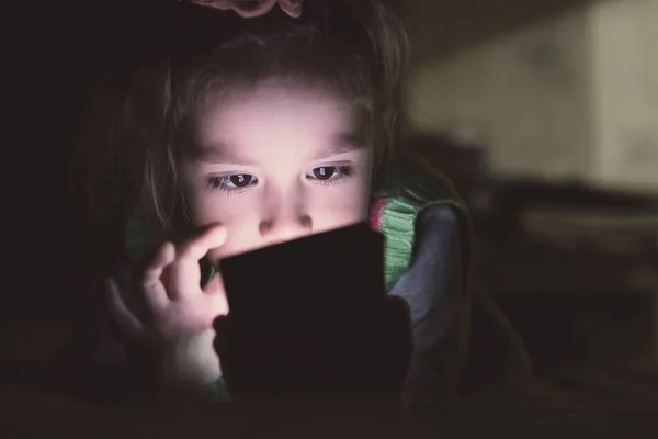 Niña con smartphone acostada en una cama , — Foto de Stock