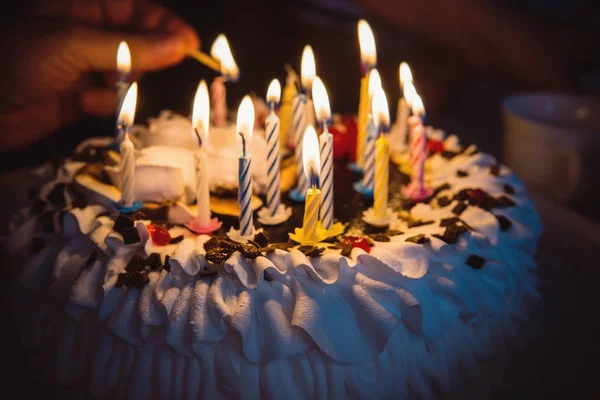 Bolo de aniversário com mão queimando velas no escuro — Fotografia de Stock