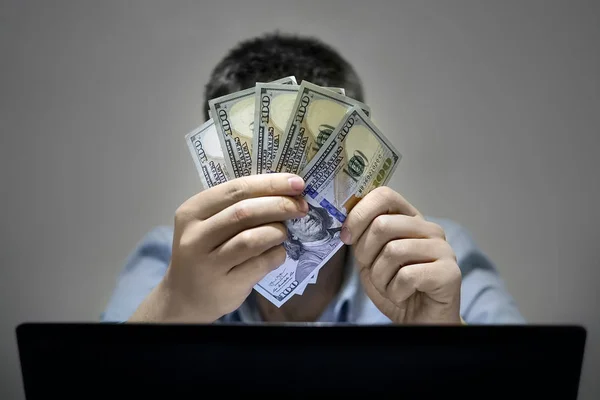 Close-up of hands shopping online using laptop while holding US dollars..