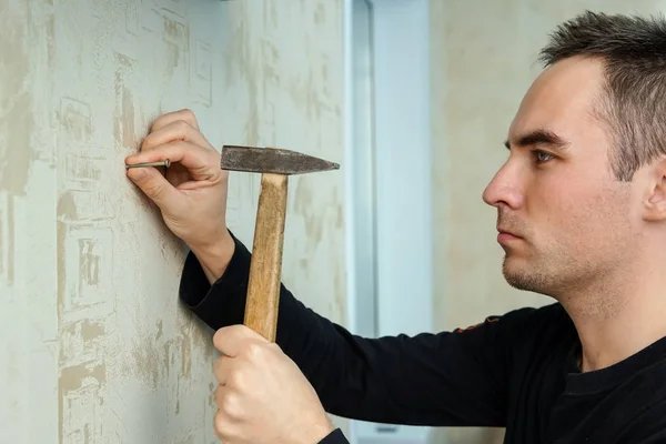 A man hammers a nail into plaster wall under the Wallpaper — Stock Photo, Image