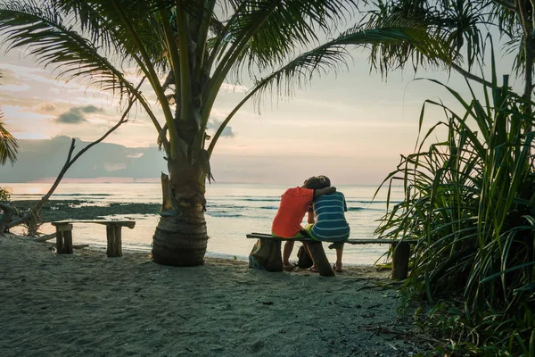 Una giovane coppia si siede su una panchina sotto una palma — Foto Stock