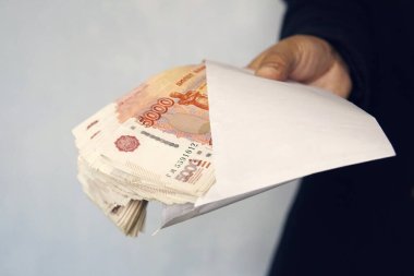 Beyaz bir zarfta 5000 ruble büyüklüğünde para var. Adam elinde para dolu bir zarf tutuyor. Rüşvet ve yolsuzluk kavramı. Nakit, nakit akışı